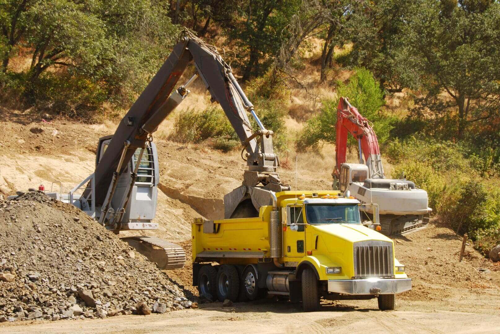 Excavators loading dirt into yellow dump truck