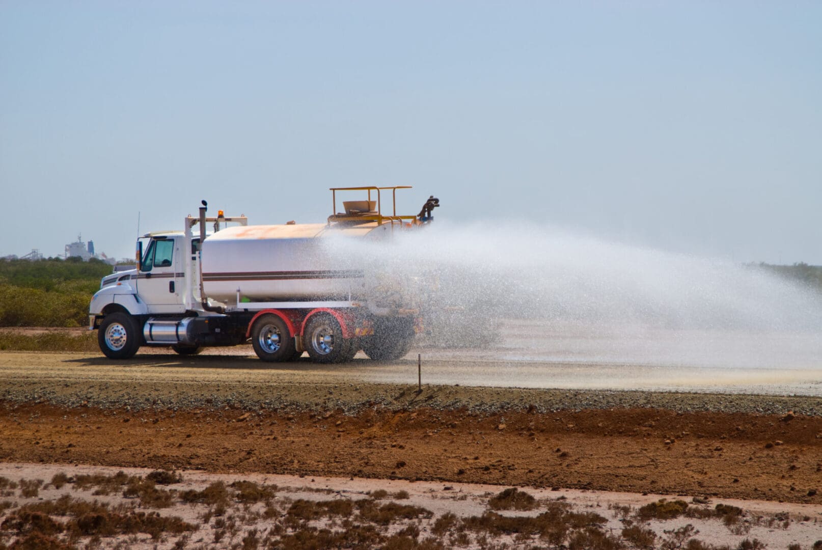Truck spraying water on dirt road.